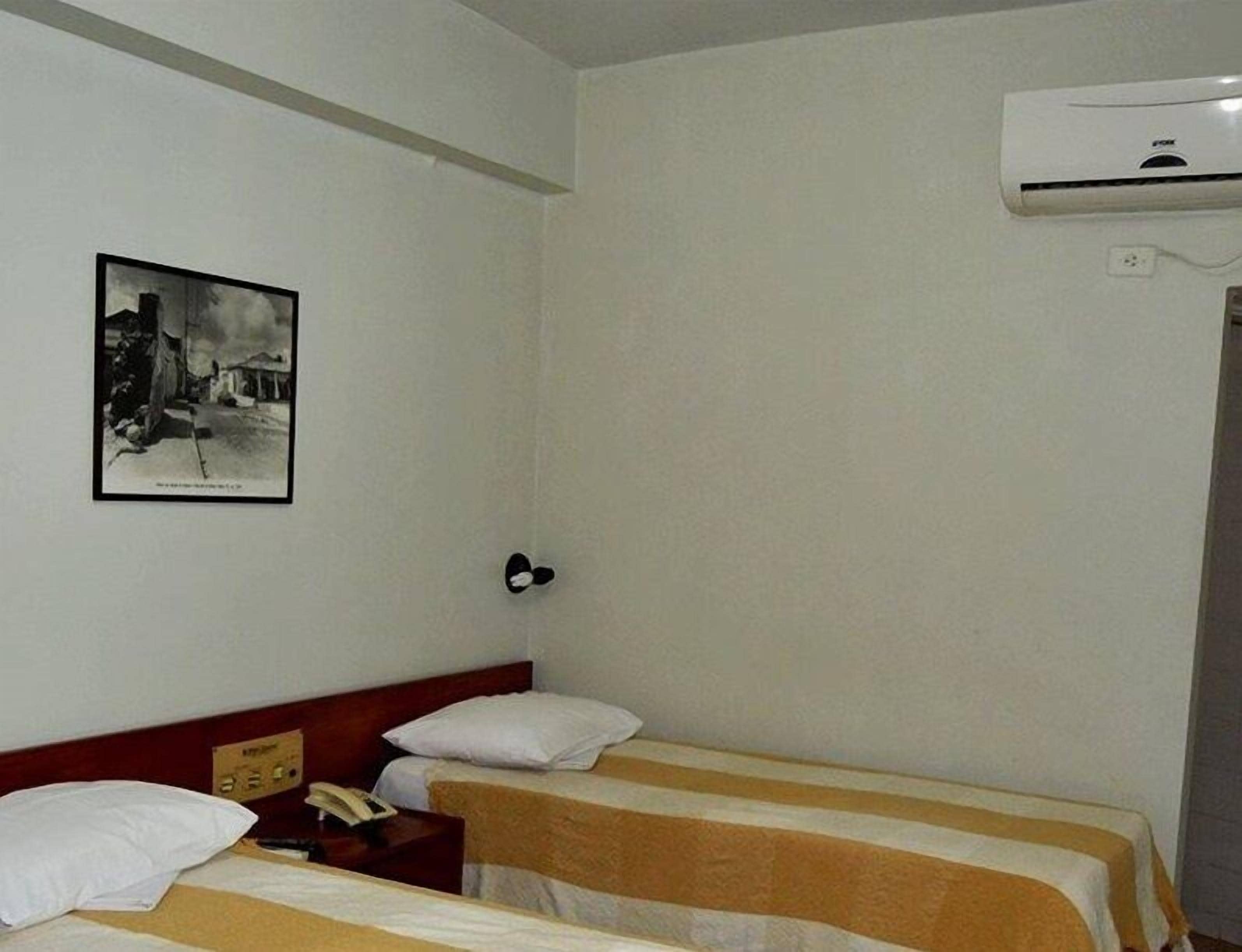 Habitación de hotel con dos camas, una mesita de noche, teléfono, aire acondicionado instalado en la pared y un cuadro enmarcado.
