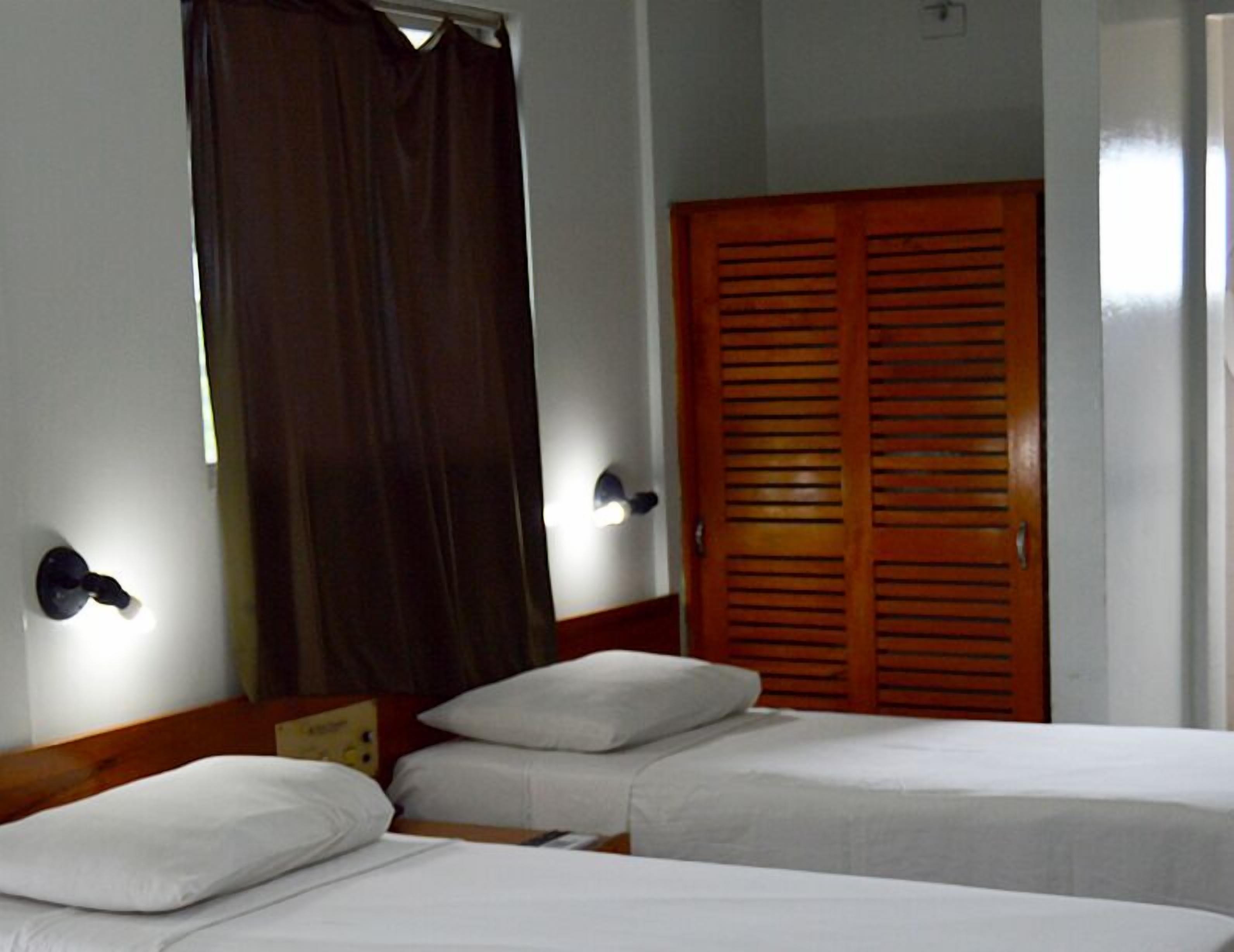 A hotel room with two single beds, a wooden door, and a curtain.