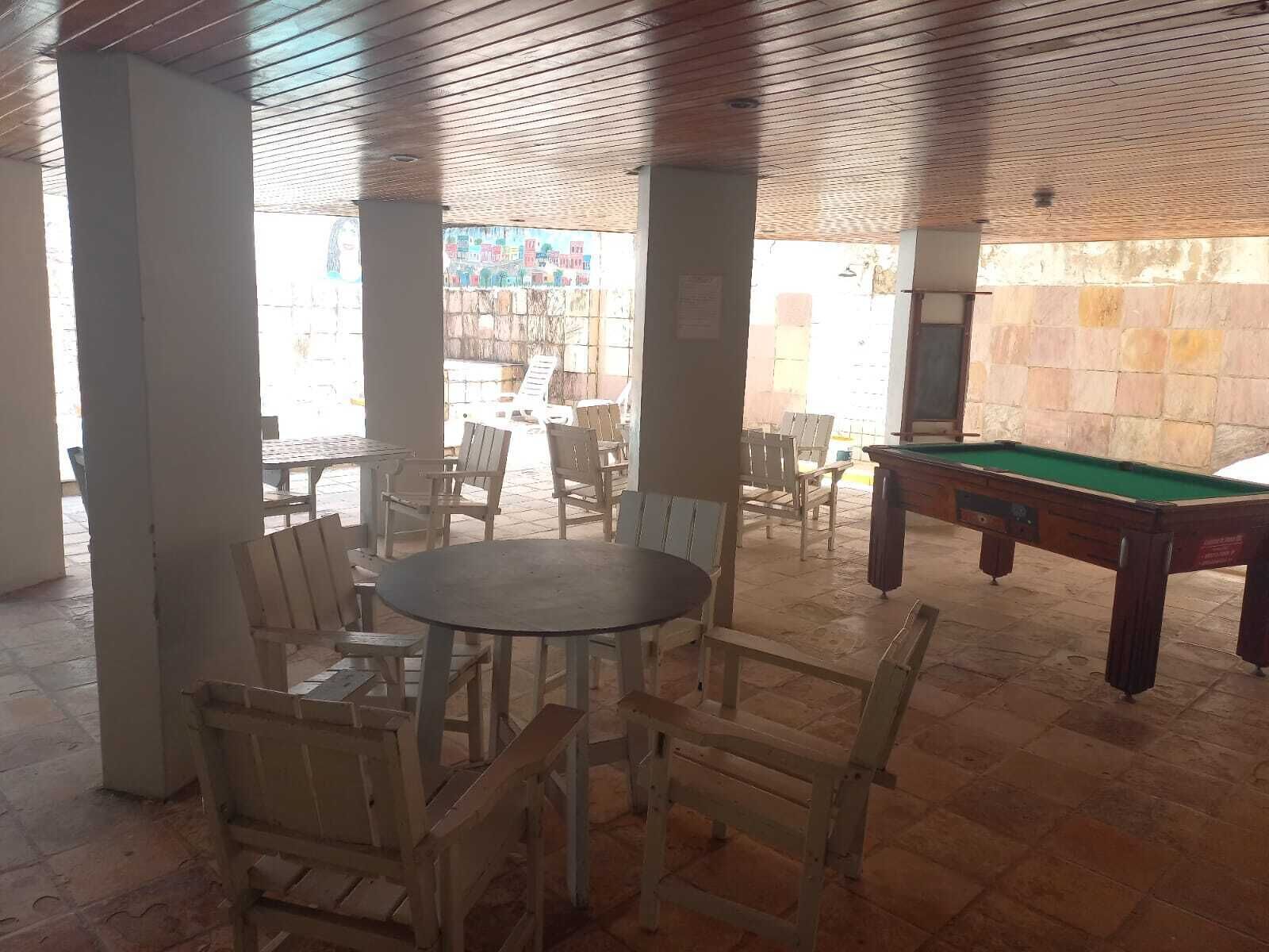 Un área de piscina interior con sillas y mesas de madera, una mesa de billar y paredes de piedra.