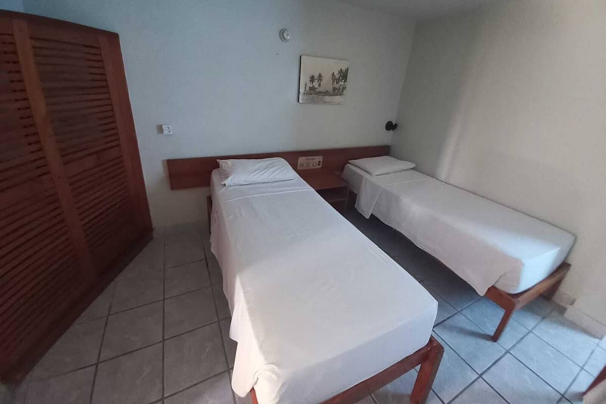 A room with two single beds, a wooden wardrobe, a wall-mounted light, and a small picture.