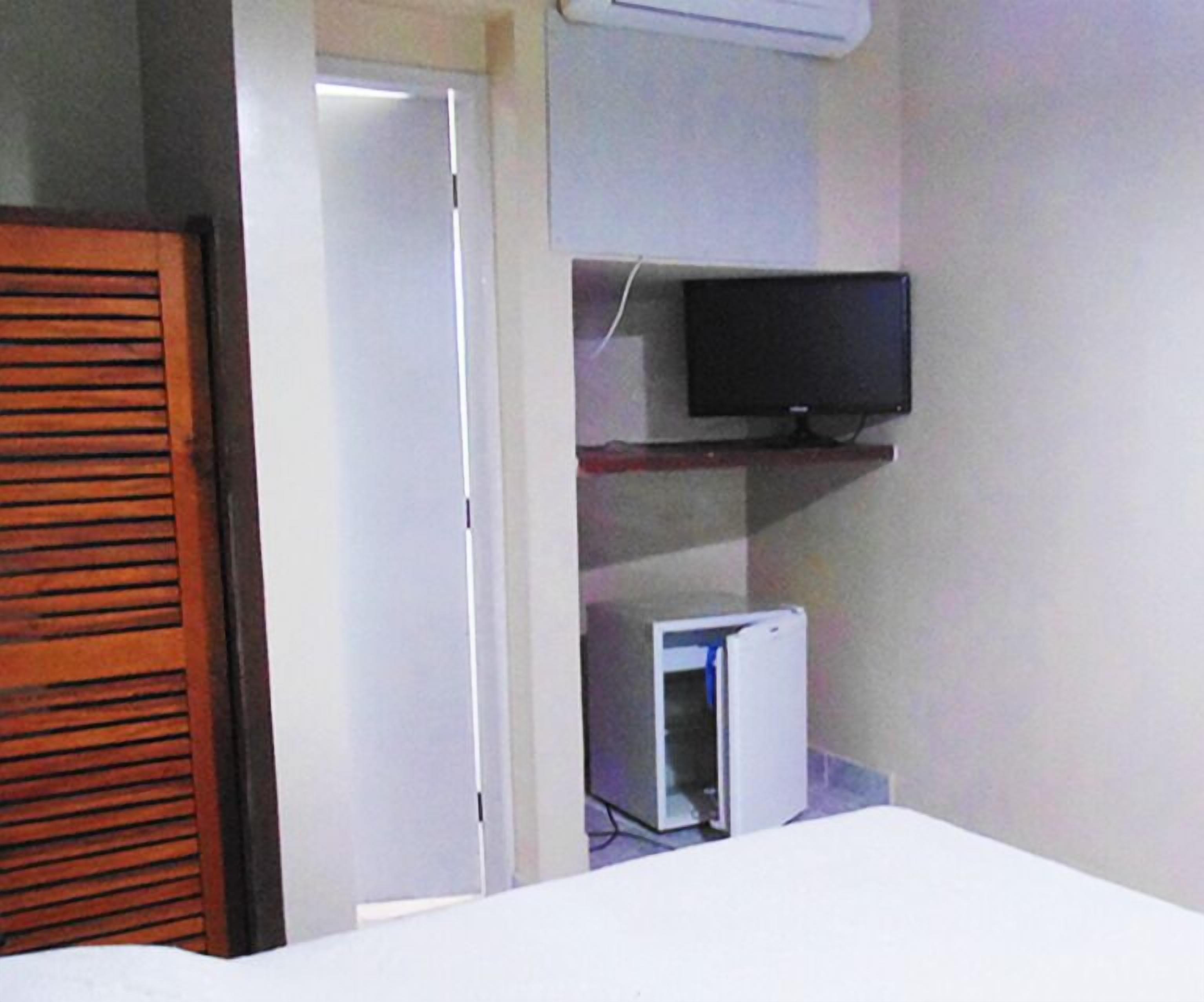 Quarto com cama, televisão numa prateleira e um frigorífico pequeno.