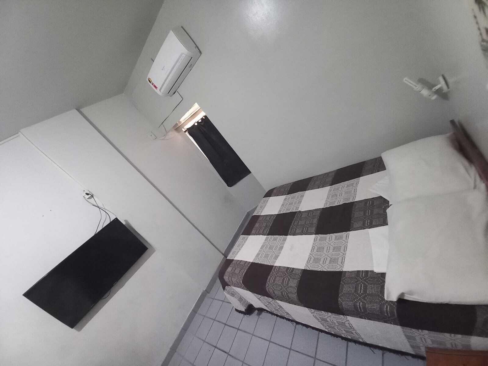 Una habitación pequeña y escasamente amoblada, con una cama, un calentador de pared y un ventanal.