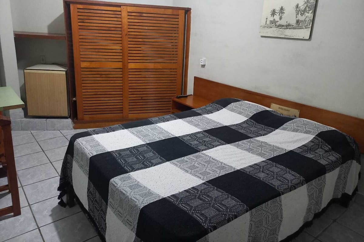 A bedroom with a bed, a wardrobe, a small table, and a wall-mounted picture.