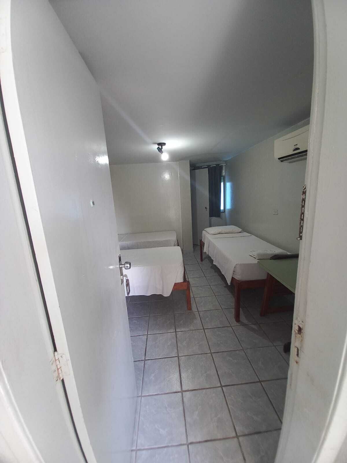 A small, clean room with two single beds, a tiled floor, and a ceiling light.