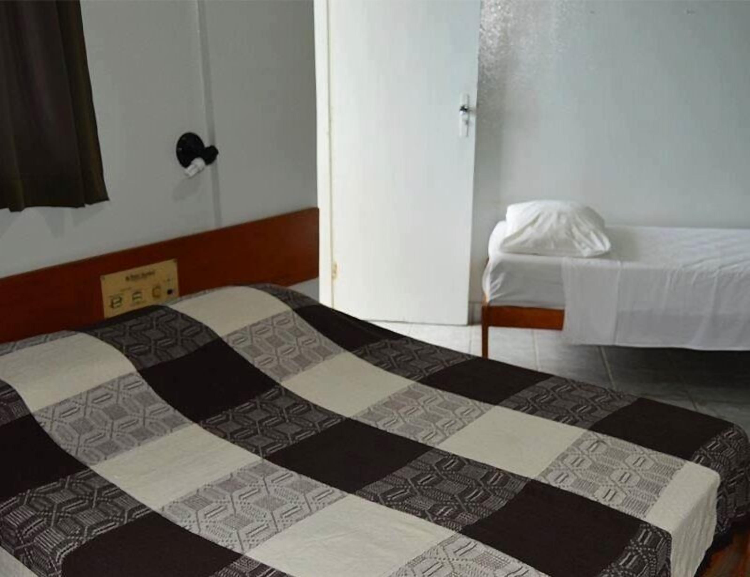 A hotel room with a bed, a bedside table, a door, and a sign on the wall.
