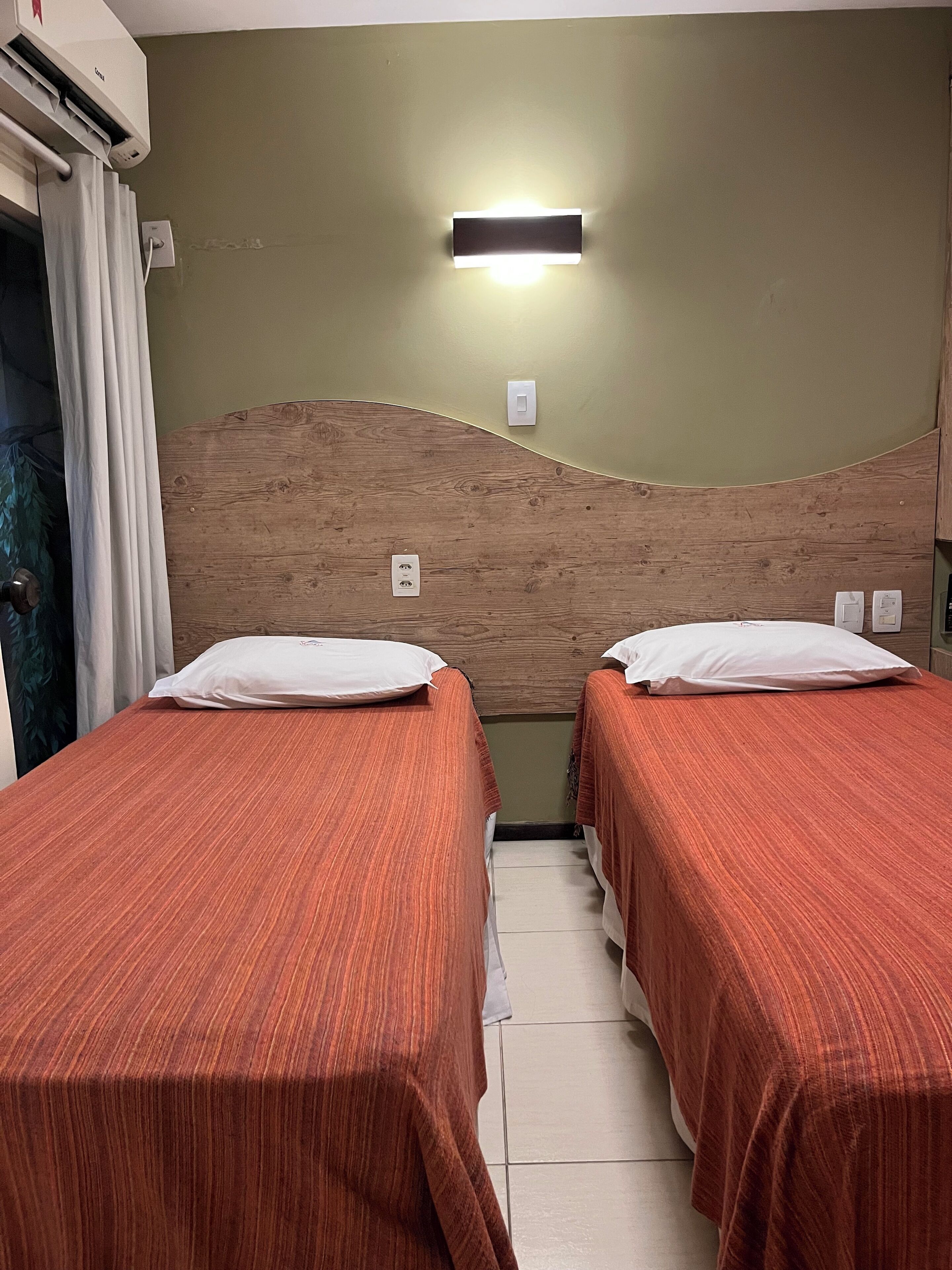 Una habitación con dos camas, un cabecero de madera, una lámpara de pared y un equipo de aire acondicionado.