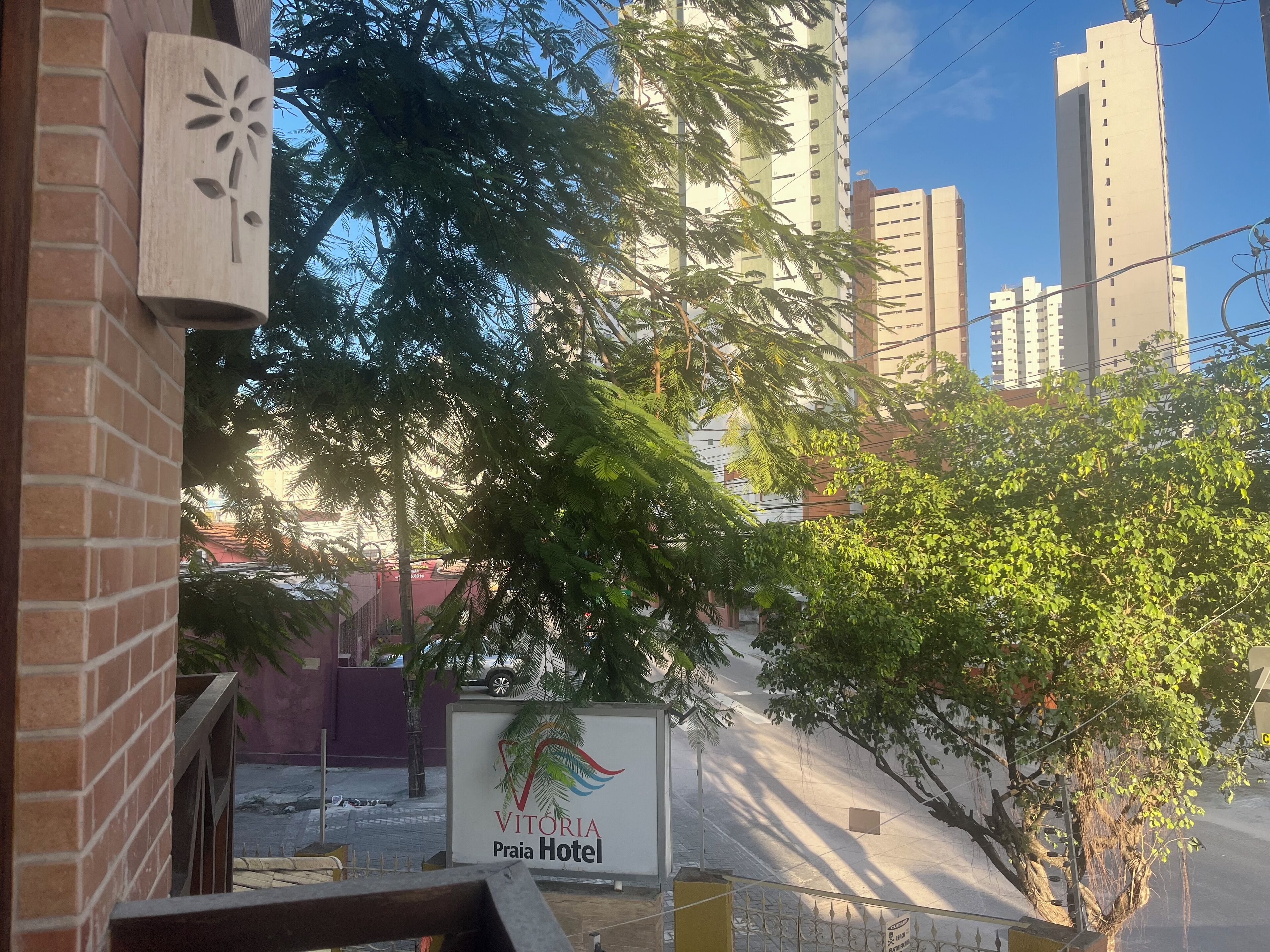 A sign for Vitoria Praia Hotel with a view of tall buildings and trees in the background.