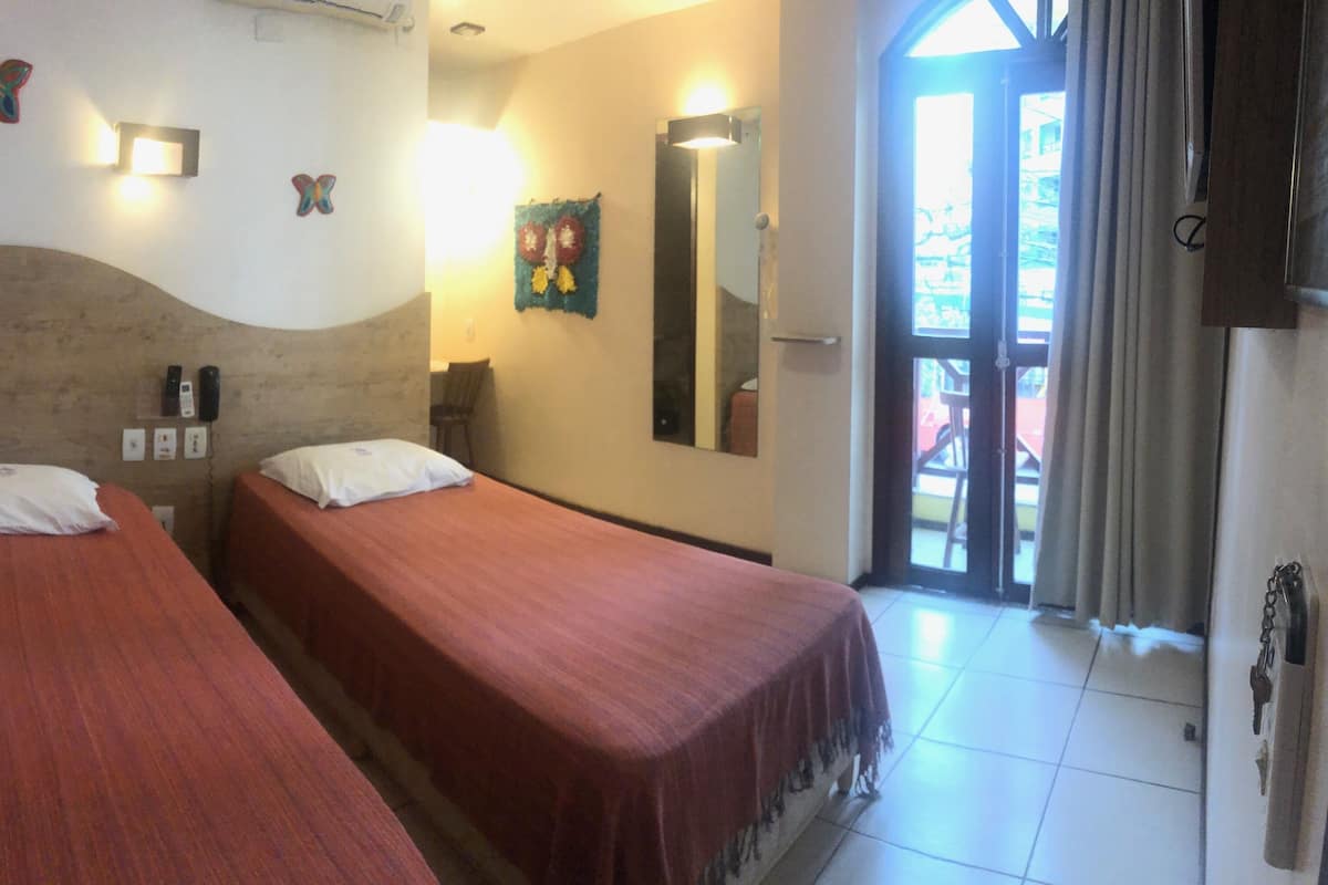 A room with two single beds, a wooden headboard, a wall-mounted mirror, and a door leading to an outdoor area.