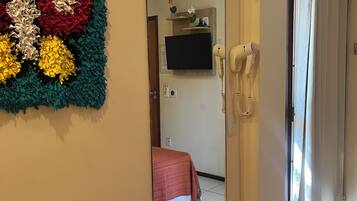 Habitación de hotel con un espejo grande, un televisor de pared, un secador de pelo y un cesto de basura.