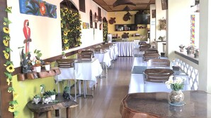A restaurant with a long counter, multiple tables, and chairs. There are potted plants and wall art. - Vitória Praia Hotel (Recife)