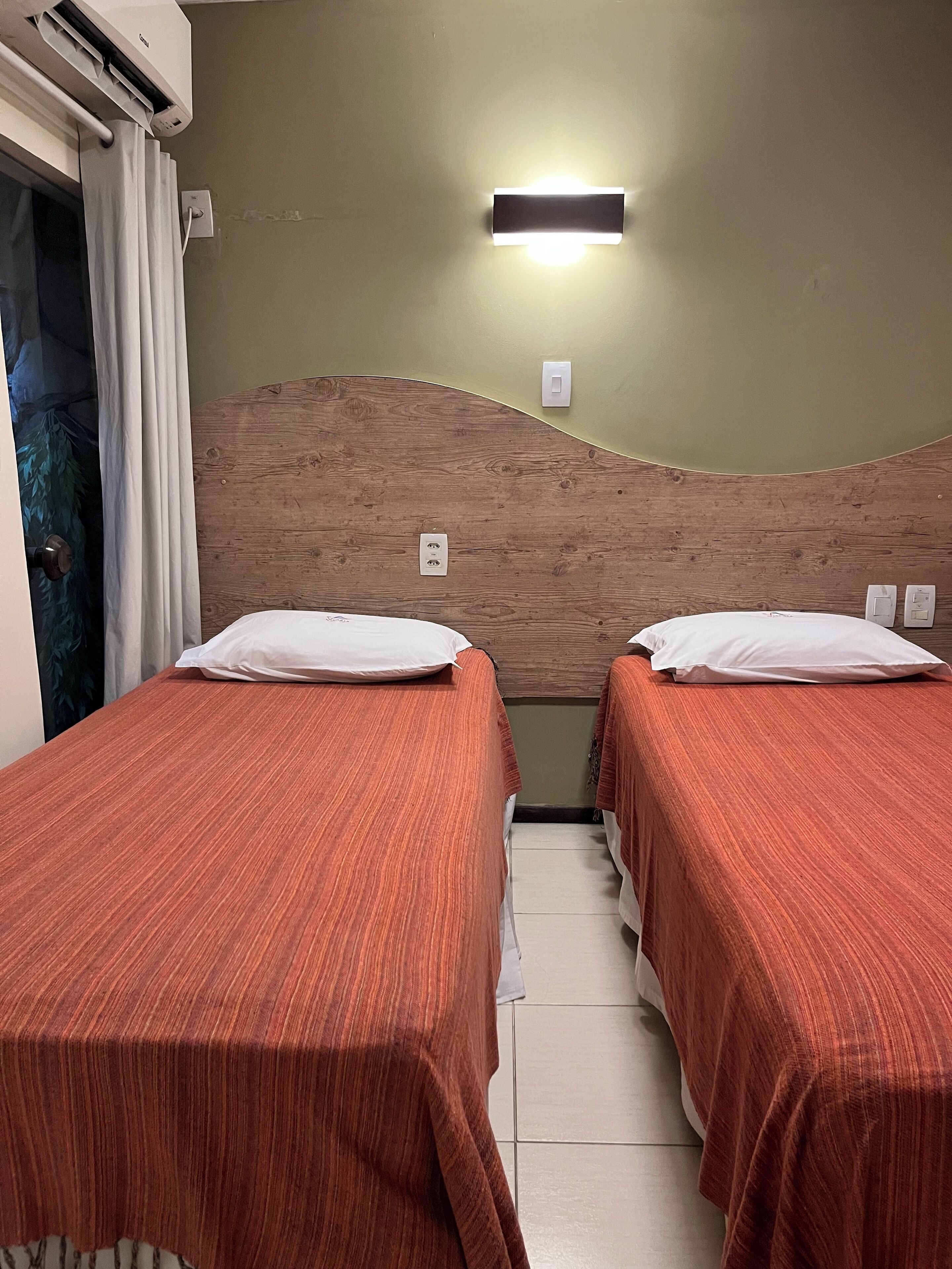 Una habitación con dos camas, cabecero de madera, luz empotrada en la pared y equipo de aire acondicionado.