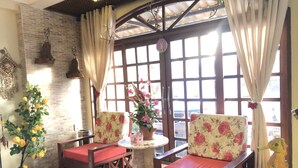 A cozy room with two wooden chairs with red cushions, a small round table, and a potted plant. - Vitória Praia Hotel (Recife)