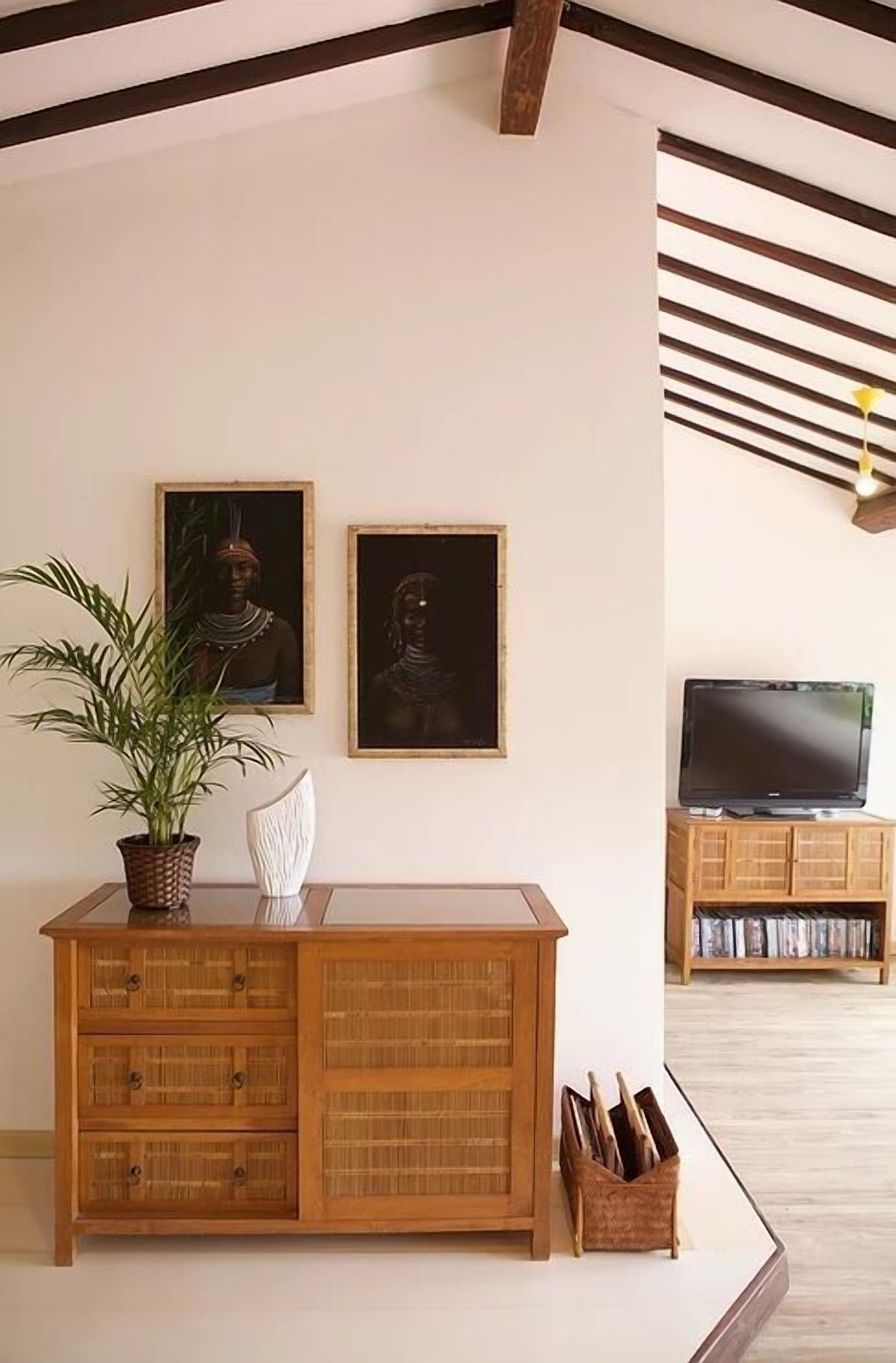A living room with a wooden cabinet, a potted plant, and two framed pictures on the wall.