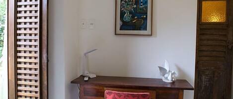 A room with a wooden desk, a white desk lamp, a framed painting, and a decorative sculpture.