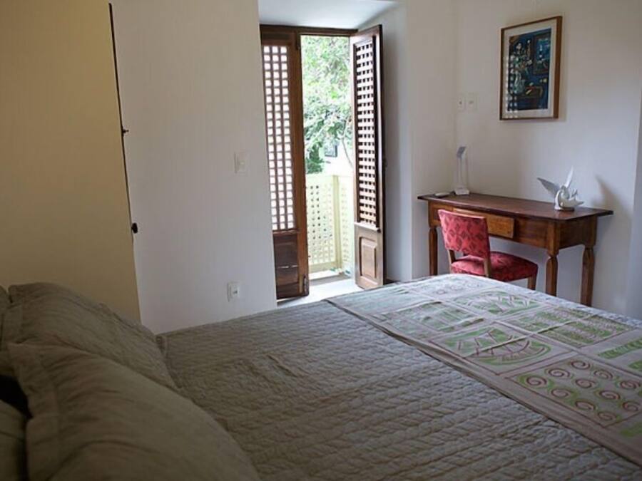Une chambre avec un lit, un bureau et une chaise. Une porte donne accès à un espace extérieur.