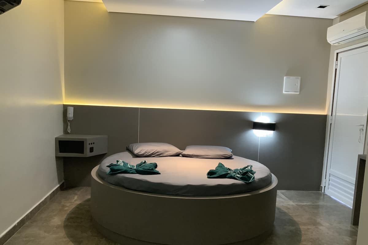 Un lit moderne de forme circulaire, doté d’une tête de lit, d’une table de chevet avec une lampe et d’un climatiseur fixé au mur.