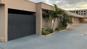 Un edificio moderno con fachada color beige, una reja negra y una zona de estacionamiento con bordes amarillos.