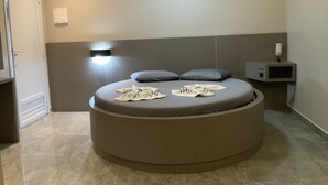 Un dormitorio moderno con cama redonda, mesita de noche, luz empotrada en la pared y televisor integrado.