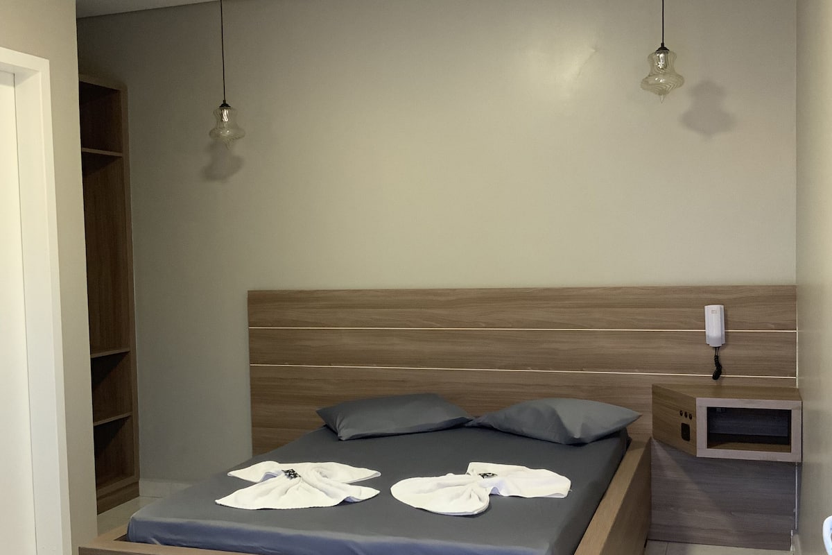 Une chambre moderne avec un lit en bois, une literie grise et une table de chevet sur laquelle se trouve un téléphone.