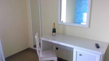 A small, clean room with a white desk, a chair, a bottle of champagne, and a mirror on the wall.