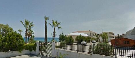 A coastal residential area with a gated entrance, palm trees, and a view of the sea.