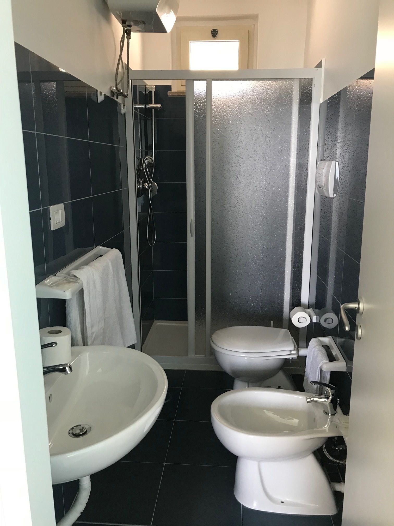 Ein kleines Badezimmer mit Duschkabine, Waschbecken und zwei Toiletten.