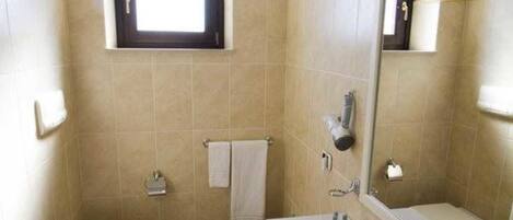 Un baño con inodoro, lavamanos y espejo. Hay un perchero para toallas y una ventana sobre el inodoro.