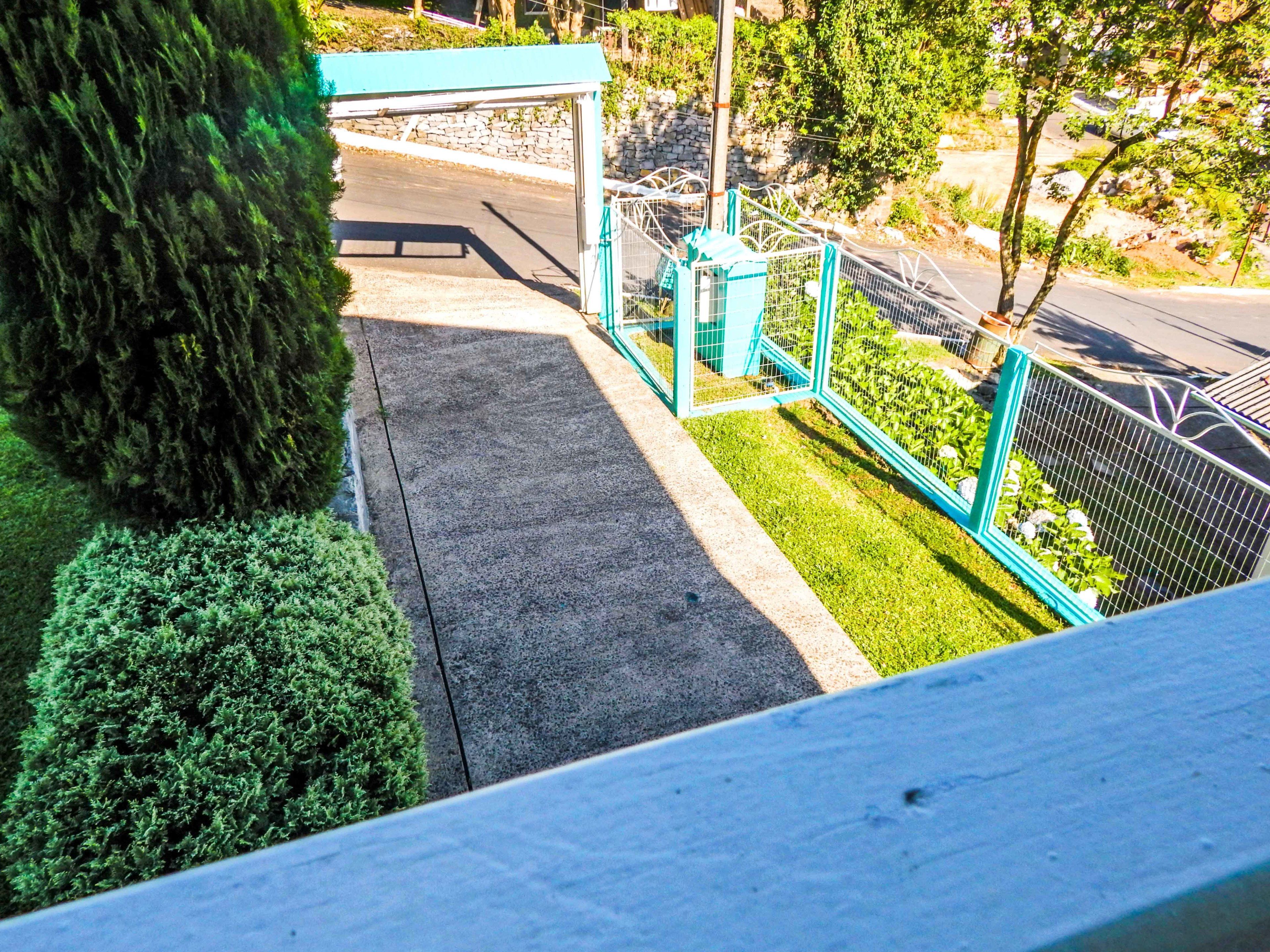 A view of a parking area with a green fence, a stone wall, and a covered area.