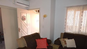 A living room with two sofas, a door with a decorative wreath, and a window with patterned curtains. - Apartamento dos Altos Centro de Gramado (Gramado)