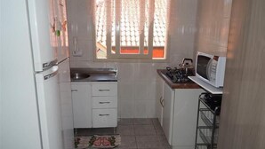 A compact kitchen with white cabinets, a gas stove, a microwave, and a refrigerator. - Apartamento dos Altos Centro de Gramado (Gramado)