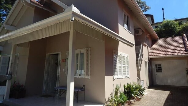 A two-story house with a covered porch, a small garden, and a garage. - Apartamento dos Altos Centro de Gramado (Gramado)