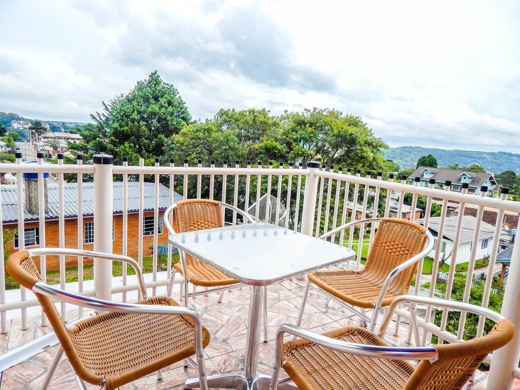 A balcony with wicker chairs and a table, overlooking a residential area with houses and greenery.