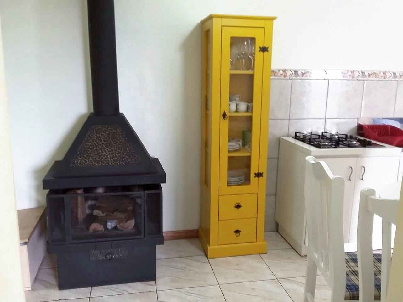 A kitchen with a black wood stove, a yellow cabinet, and a white chair.