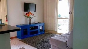 Ein Wohnzimmer mit flachbildfernseher an der Wand, einer blauen Unterhaltungsecke, einem grauen Sofa und einem großen Fenster mit Vorhängen.