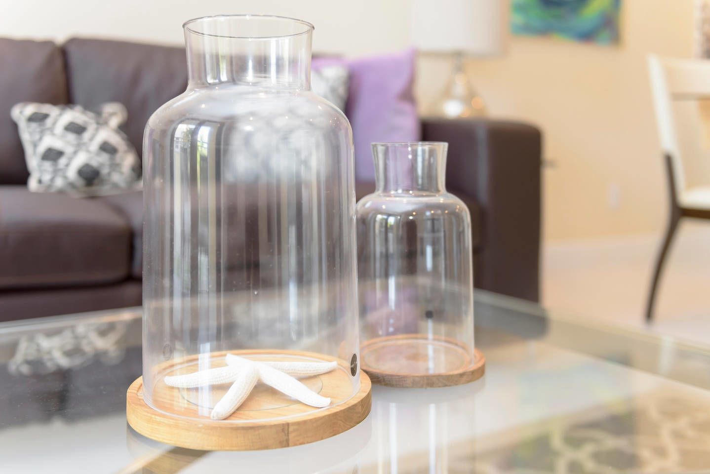 Two glass vases on a glass table, one larger than the other, with a starfish on the larger vase.