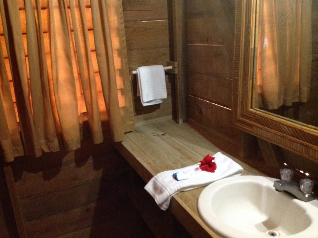 Une salle de bain avec un plancher en bois, un lavabo blanc et un miroir doté d’un cadre en bois.