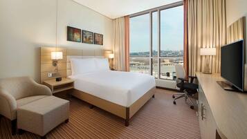 Een hotelkamer met een groot bed, een bureau met stoel, een televisie en uitzicht op de stad door het raam.