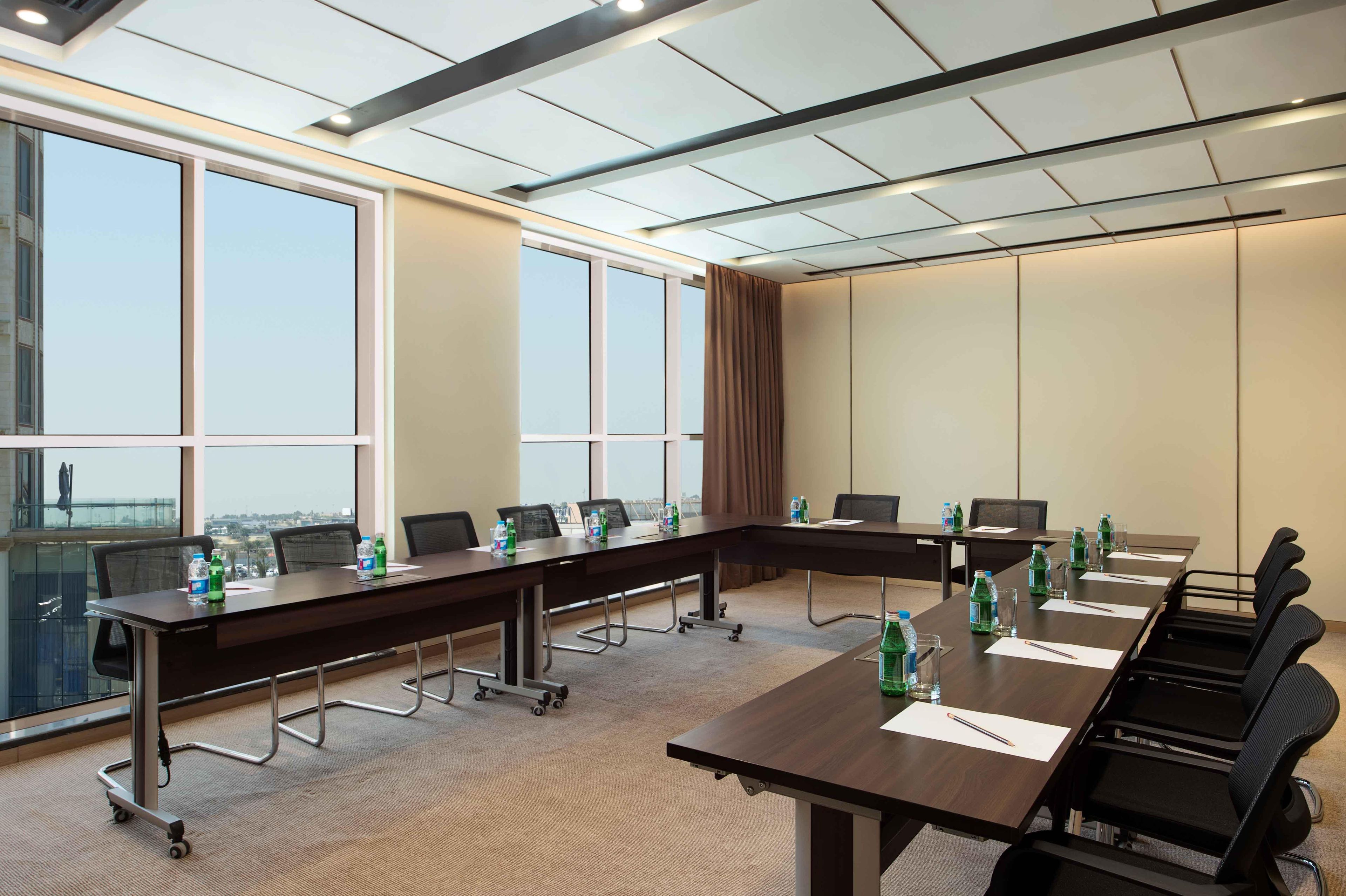 A conference room with a long table, chairs, water bottles, and a view through large windows.