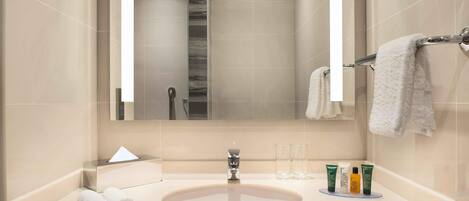 Un bagno moderno con uno specchio grande, un lavandino, due asciugamani e articoli da toilette sul ripiano.