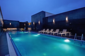 A swimming pool with lounge chairs and a modern building in the background. - Hilton Garden Inn Al Khobar (Al Khobar)