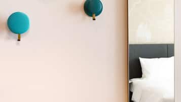 Eine Wand mit drei in Wandhalterungen montierten, türkisfarbenen Lampen und einem Spiegel, der ein Bett mit weißer Bettwäsche reflektiert.