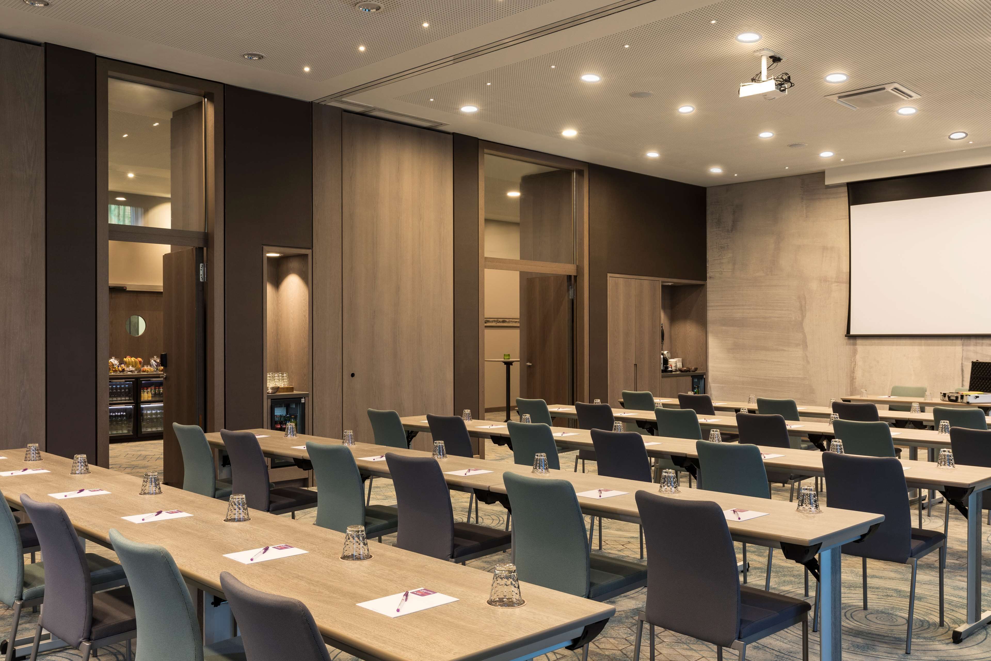 A conference room with multiple tables and chairs, a projector screen, and a large mirror on the wall.