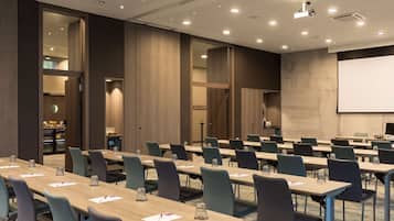 A conference room with multiple tables and chairs, a projector screen, and a large mirror on the wall.