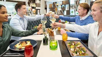 Un groupe de personnes trinquant dans un restaurant au décor moderne, qui se distingue notamment par un design de plafond original et un mobilier contemporain.
