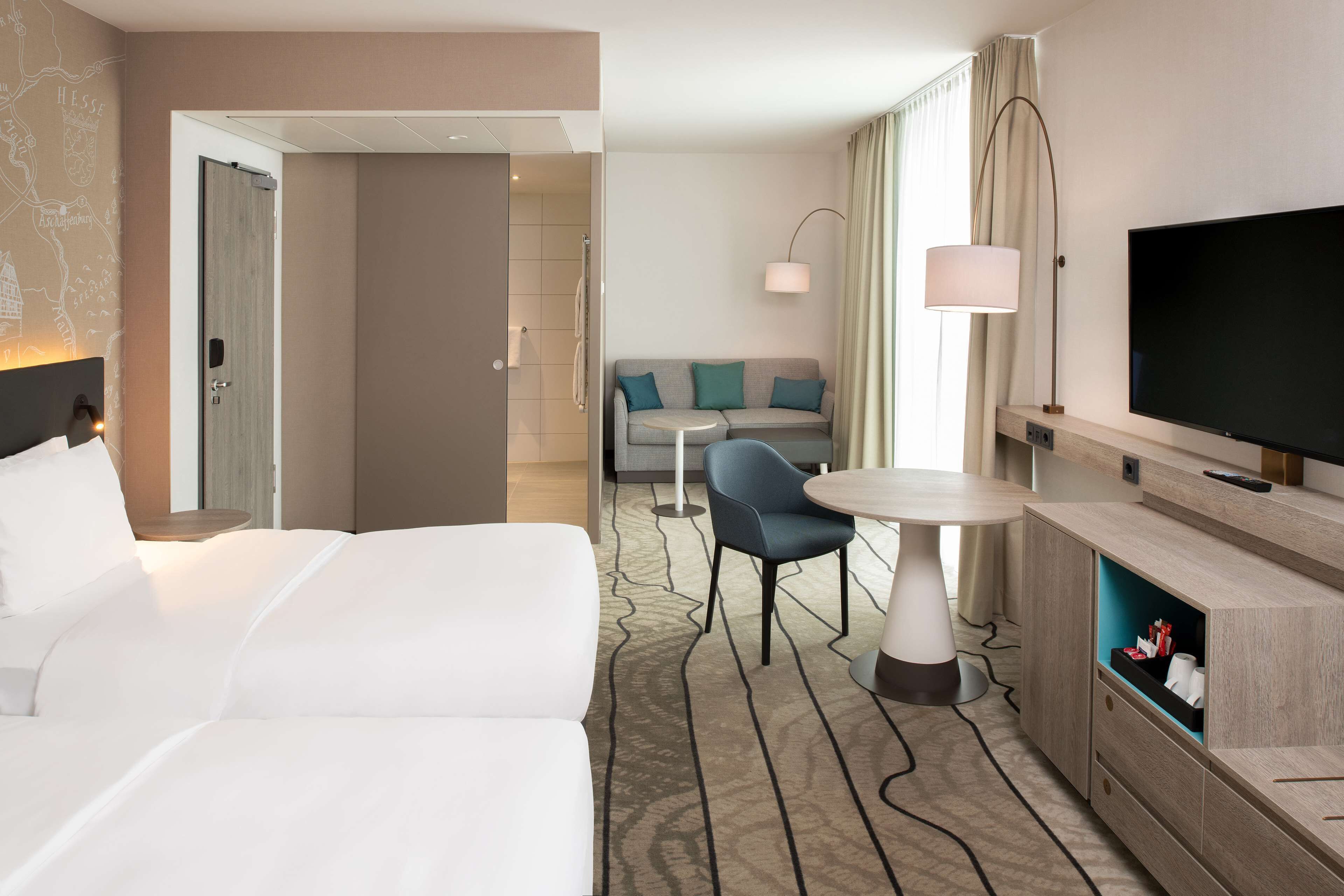 Habitació d'hotel amb un llit, un sofà, una televisió, una làmpada i una taula petita.