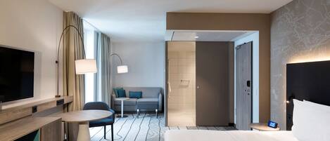 A hotel room with a bed, a TV, a desk, a sofa, and a shower area.