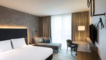 Una camera d'albergo con un letto grande, un divano, una scrivania con una sedia, una televisione e una finestra con tende.