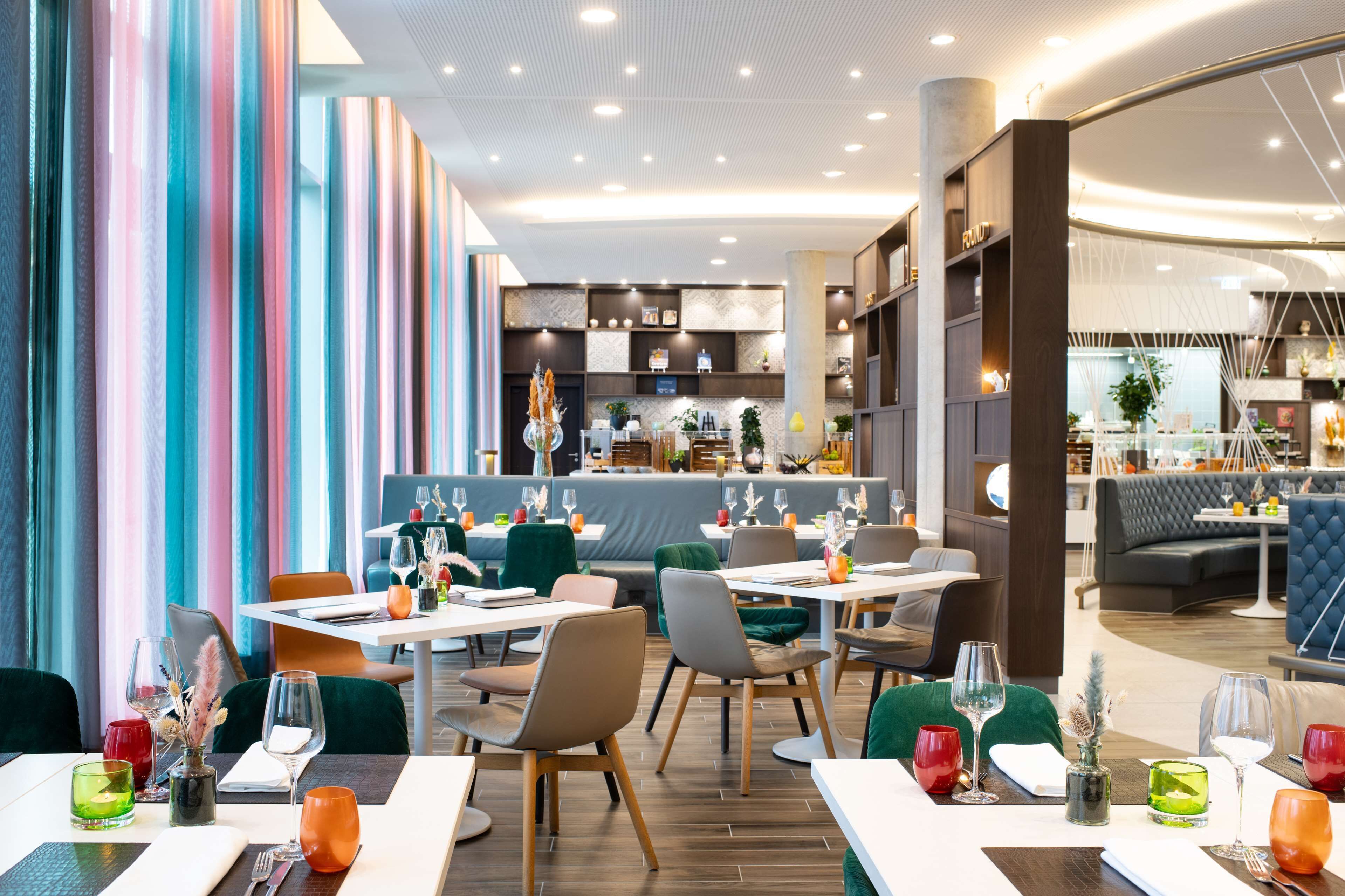 A modern restaurant interior with multiple dining tables, chairs, and a bar area.