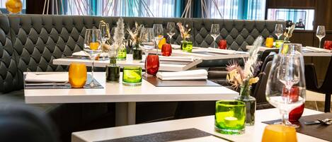 Un restaurant au décor moderne, avec des banquettes capitonnées et des tables soigneusement dressées, ornées de verres et de serviettes.