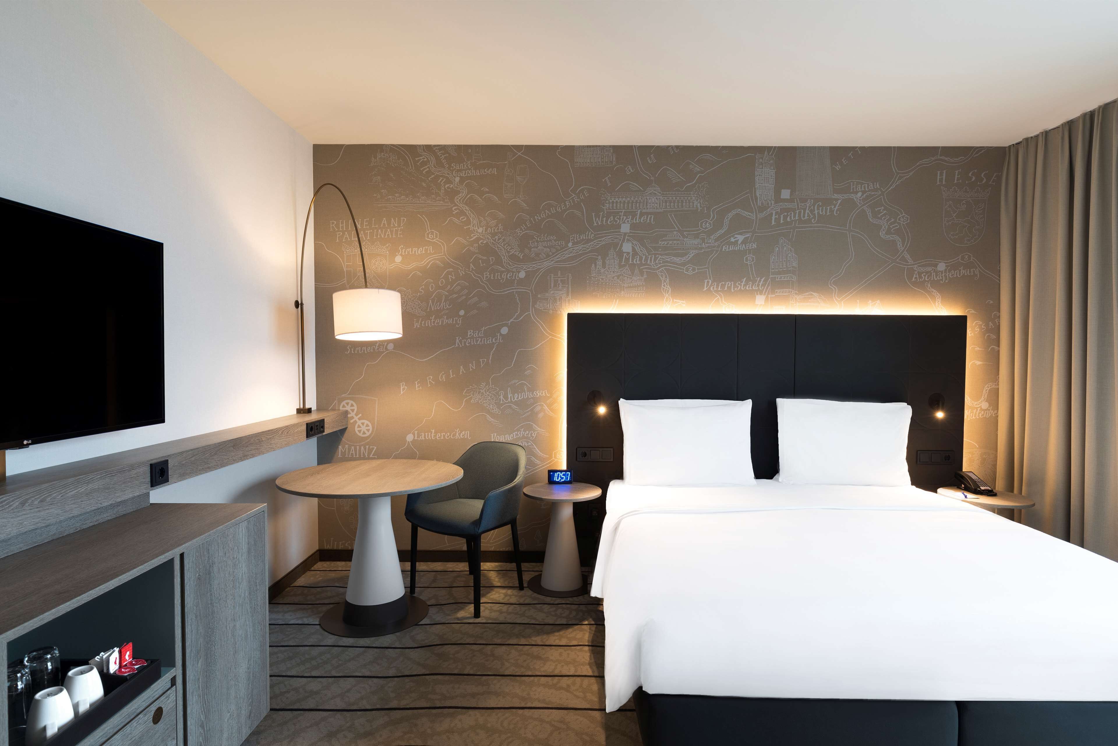 Une chambre d’hôtel avec un grand lit, un téléviseur à écran plat, un bureau avec une chaise, une petite table ronde et une carte géographique murale.